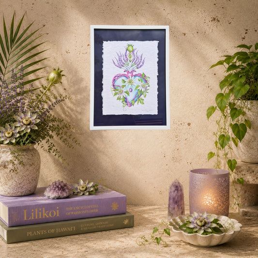 Framed artwork of a heart with flowers on a wall above books and decorative items. Framed original watercolor painting artwork with botanical sacred heart design featuring Lilikoi passion flowers and leaves on a white background of handmade paper, signed and embossed by artist Liliane Avalos