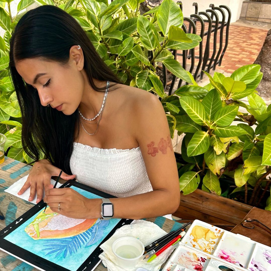 artist Liliane Avalos watercolor painting outside on bench in Waikiki Honolulu Oahu Hawaii with art supplies around her