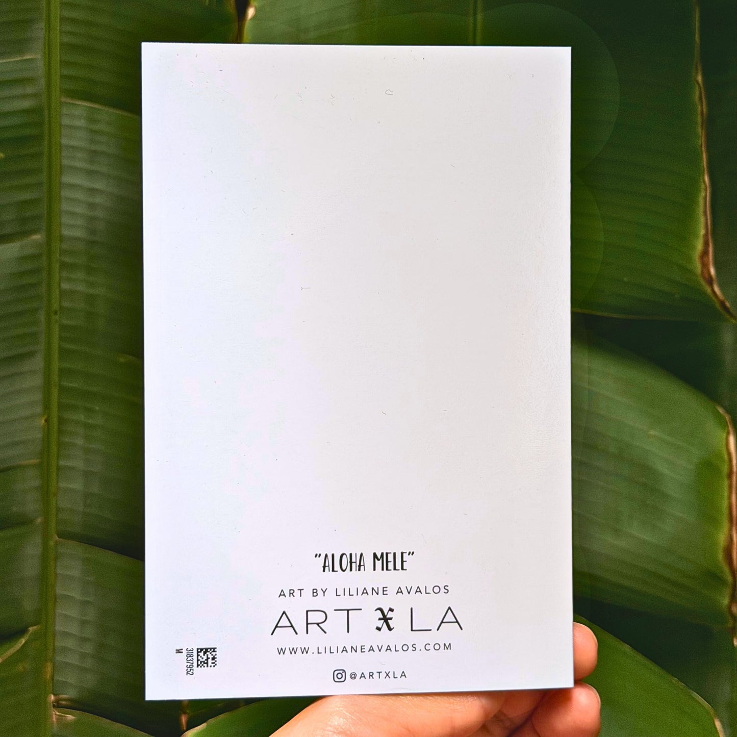 White greeting card with 'Art by LA' branding held against a green leafy background. Aloha Mele greeting card by Liliane Avalos, Kauai Hawaii artist