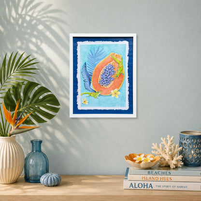 Luxury Hawaiian home with artwork of a Sunrise papaya with leaves on a wall above a table with decorative items. Framed artwork of tropical plumeria flower with palm leaves on a blue background. Good Morning Geckos, watercolor painting on handmade paper, by Liliane Avalos, Kauai Hawaii 2026. 