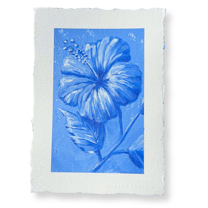 A square art print featuring a blue hibiscus flower and leaves on textured blue paper, surrounded by a wide white border with torn edges. The artist's name, Liliane Avalos, is printed at the bottom.