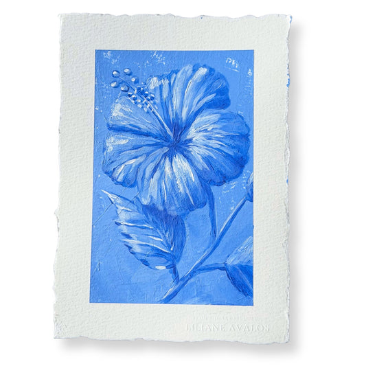 A square art print featuring a blue hibiscus flower and leaves on textured blue paper, surrounded by a wide white border with torn edges. The artist's name, Liliane Avalos, is printed at the bottom.