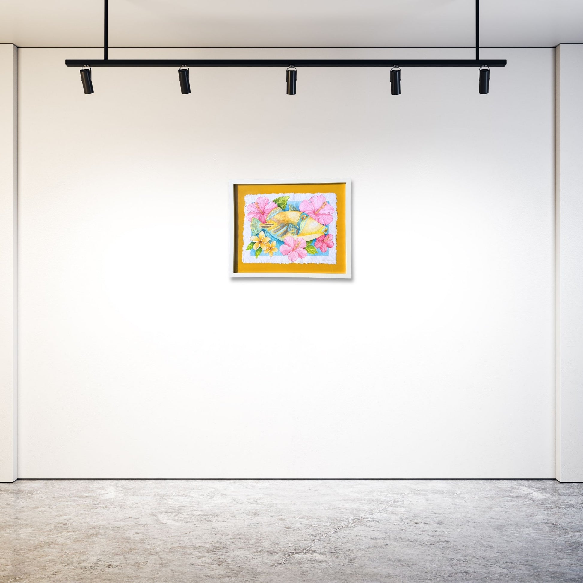 Colorful watercolor painting on a white gallery wall with modern lighting fixtures. Original watercolor painting of Humuhumunukunukuapua'a in white frame of bright colorful yellow Trigger fish surrounded by pink botanical hibiscus flowers and yellow plumeria flowers on a yellow 