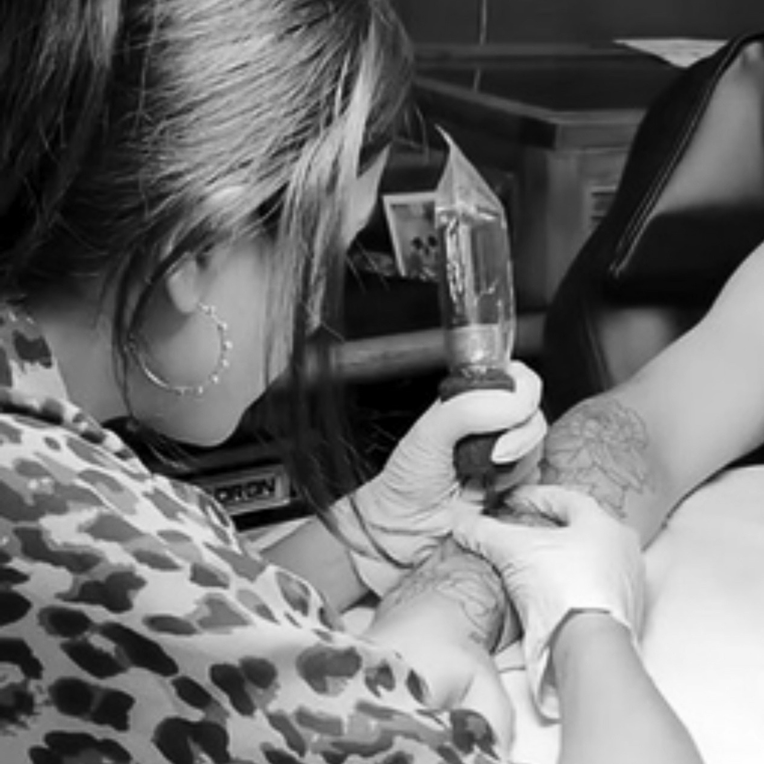 Kauai Hawaii tattoo artist Liliane Avalos with long dark hair and tattoos holding her hair, with illustrated hands in the background on a black background
Person getting a tattoo in a car interior