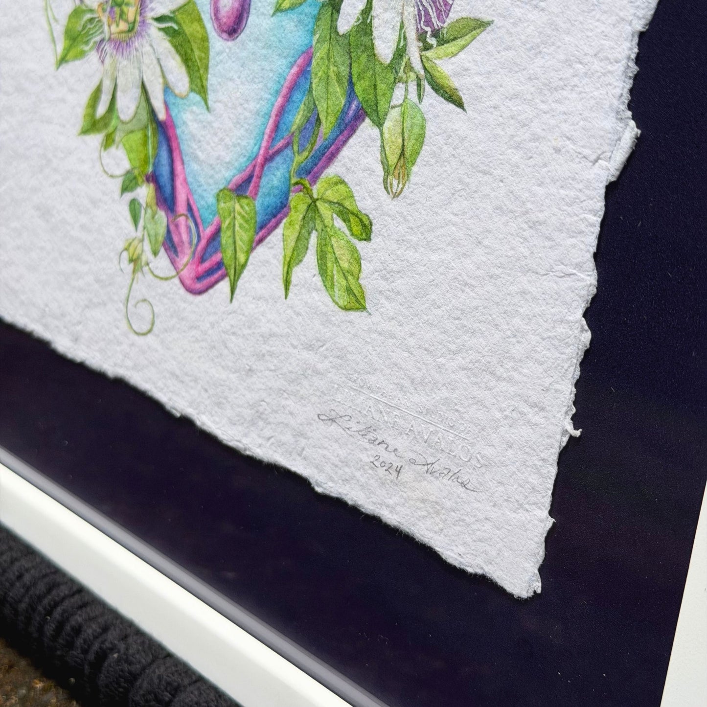Artistic depiction of a heart with floral elements on textured paper. Framed original watercolor painting artwork with botanical sacred heart design featuring Lilikoi passion flowers and leaves on a white background of handmade paper, signed and embossed by artist Liliane Avalos