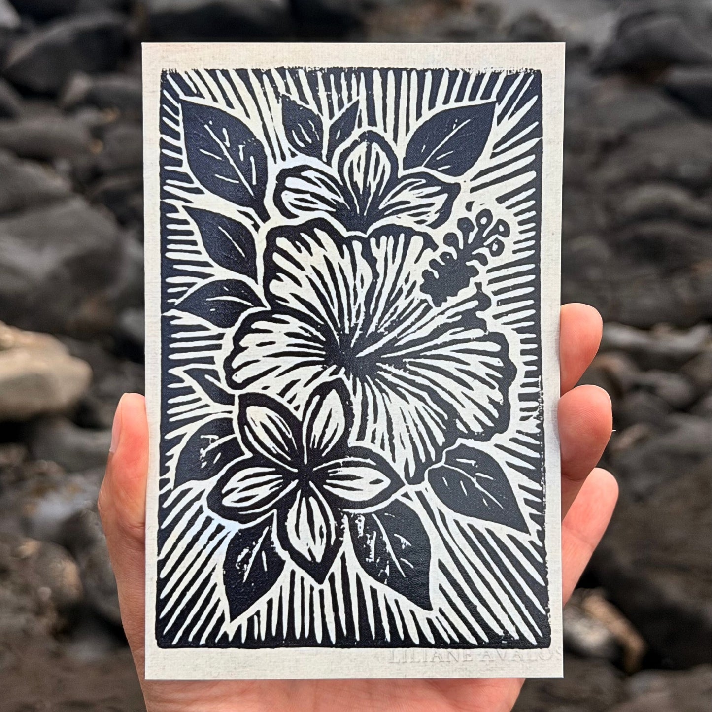 Hand holding a card with black floral design against a rocky background