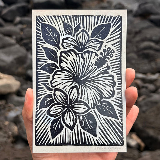 Hand holding a card with black floral design against a rocky background