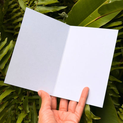 Hand holding a white notebook against a green leafy background. greeting card by Liliane Avalos, Kauai Hawaii artist